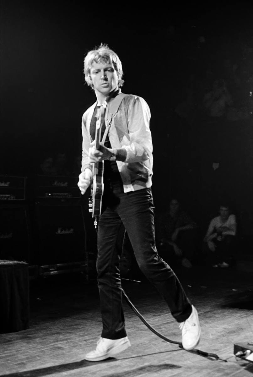 Andy Summers standing with a guitar on a dark stage, in black and white