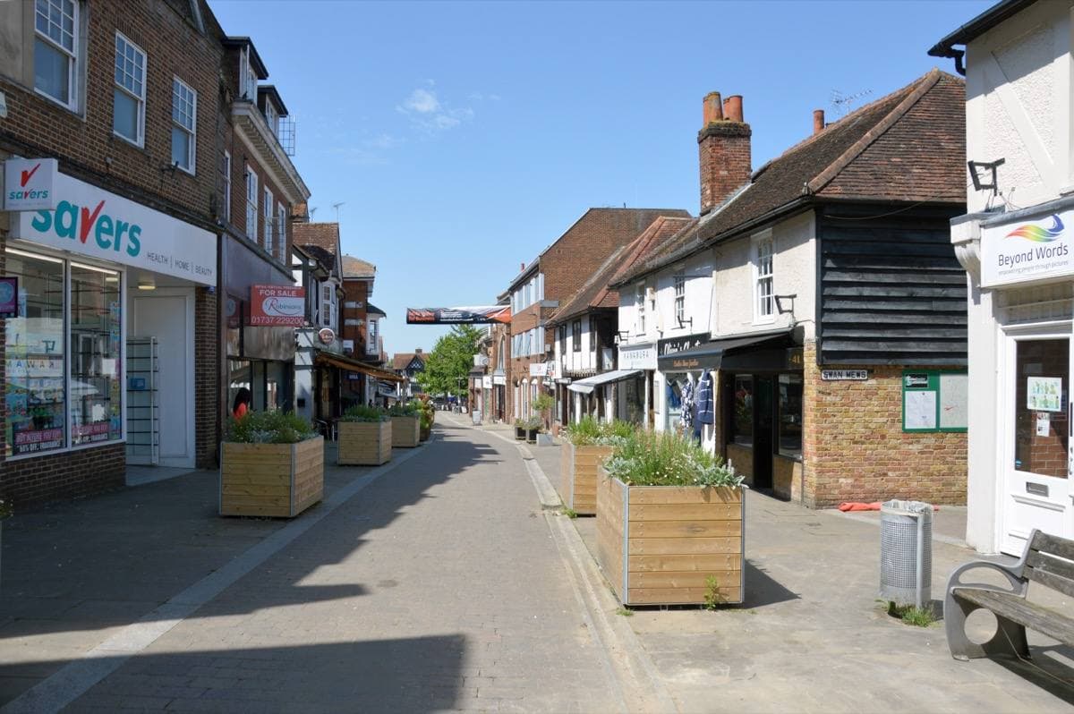 A pedestrian high street of brick shops in summer