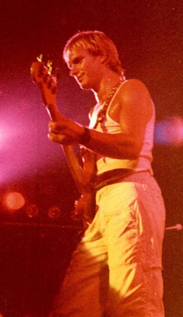 Sting in a sleeveless top playing bass under orange stage light