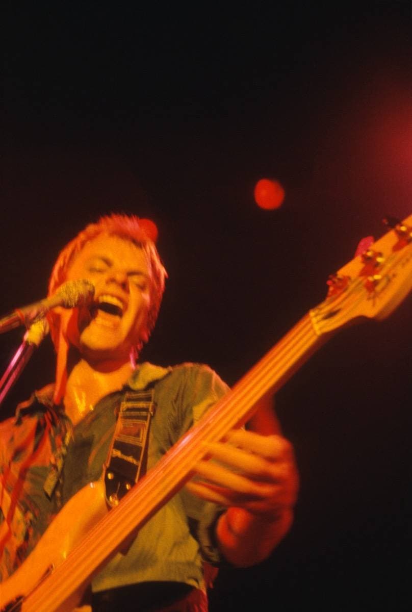Sting laughing at the microphone with his bass, lit red