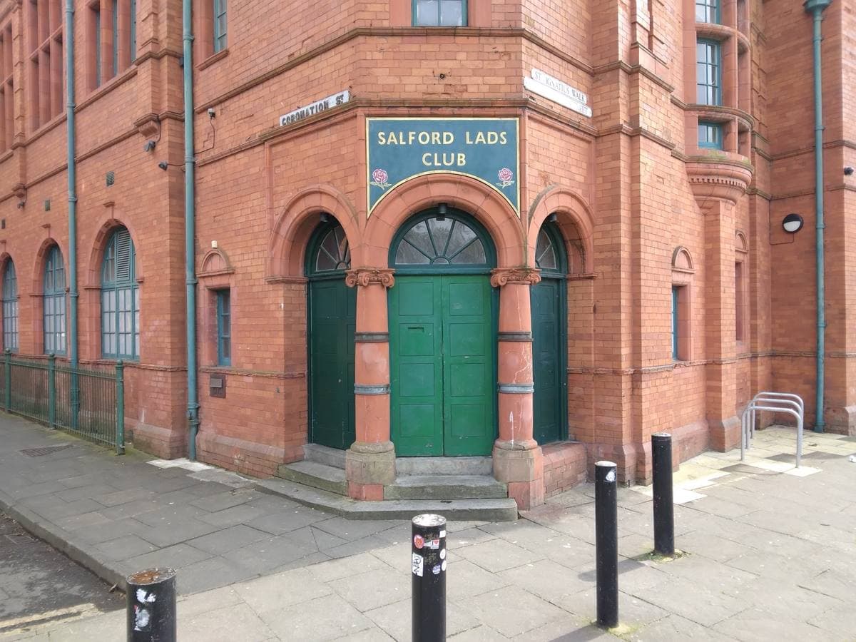 The red-brick corner entrance of Salford Lads Club, green double doors under its sign