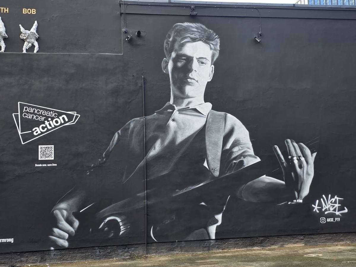 A huge black-and-white painted portrait of Andy Rourke with his bass on a black pub wall