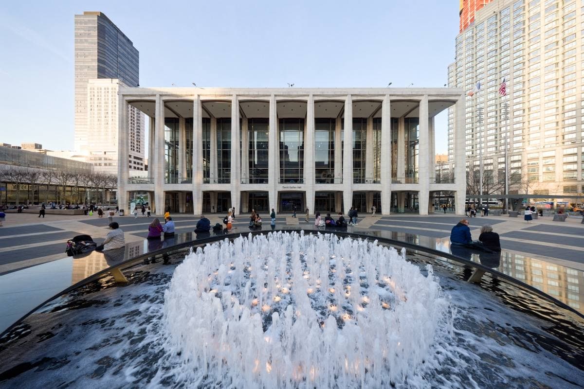 David Geffen Hall lit at dusk behind the Lincoln Center fountain