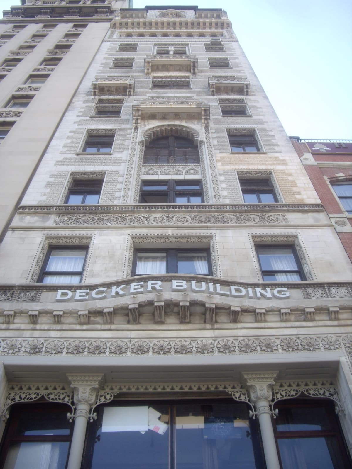 A tall, ornate pale stone building seen from below, with DECKER BUILDING carved over the entrance