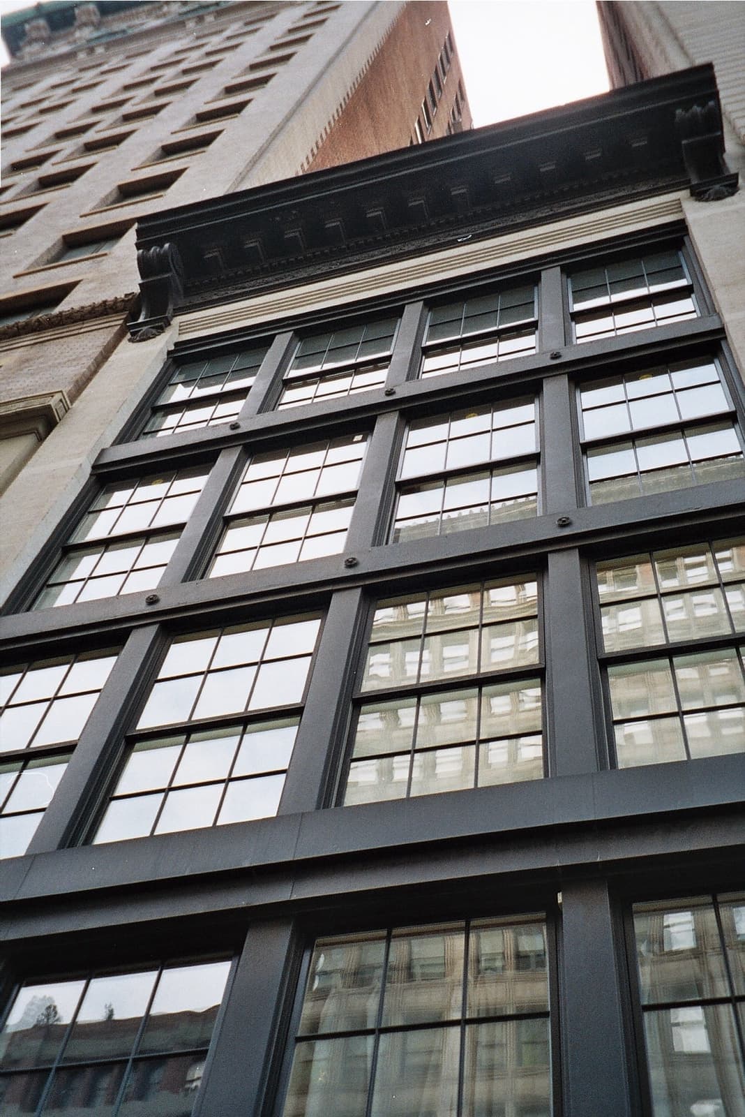 Looking up the dark facade of a corner building with tall windows on Park Avenue South