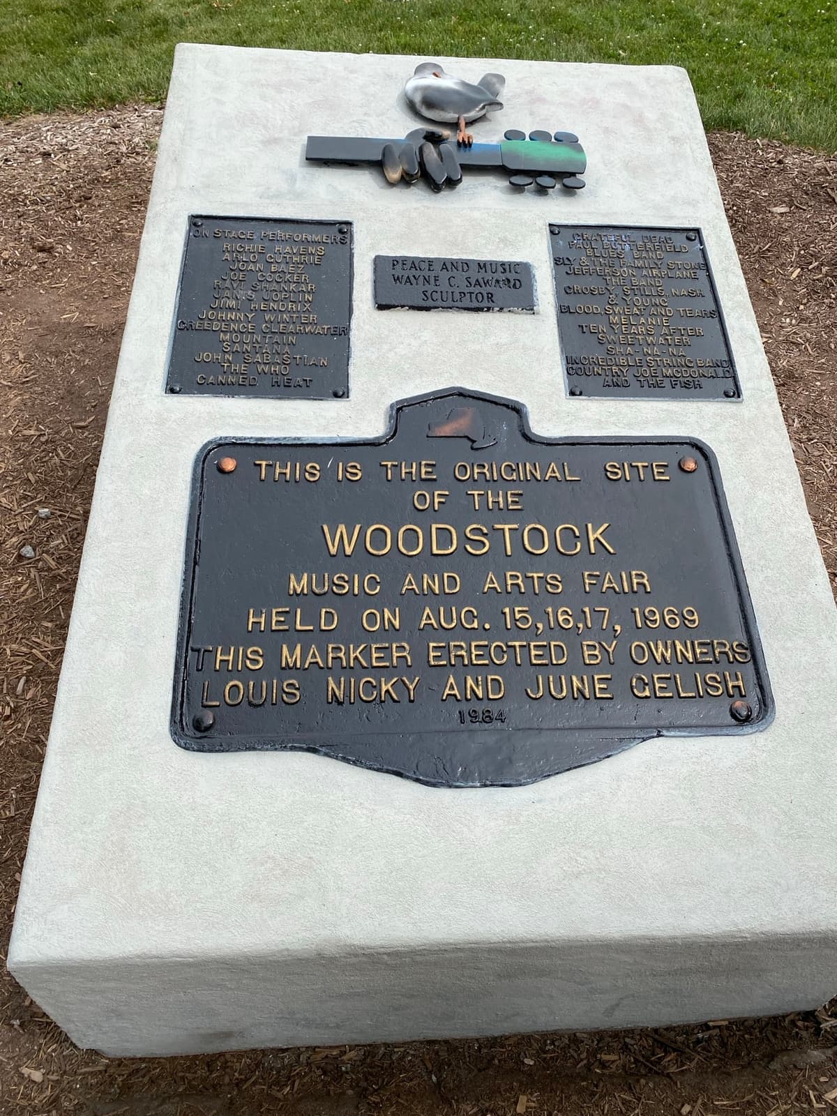 A stone marker with bronze plaques on the edge of a grass field