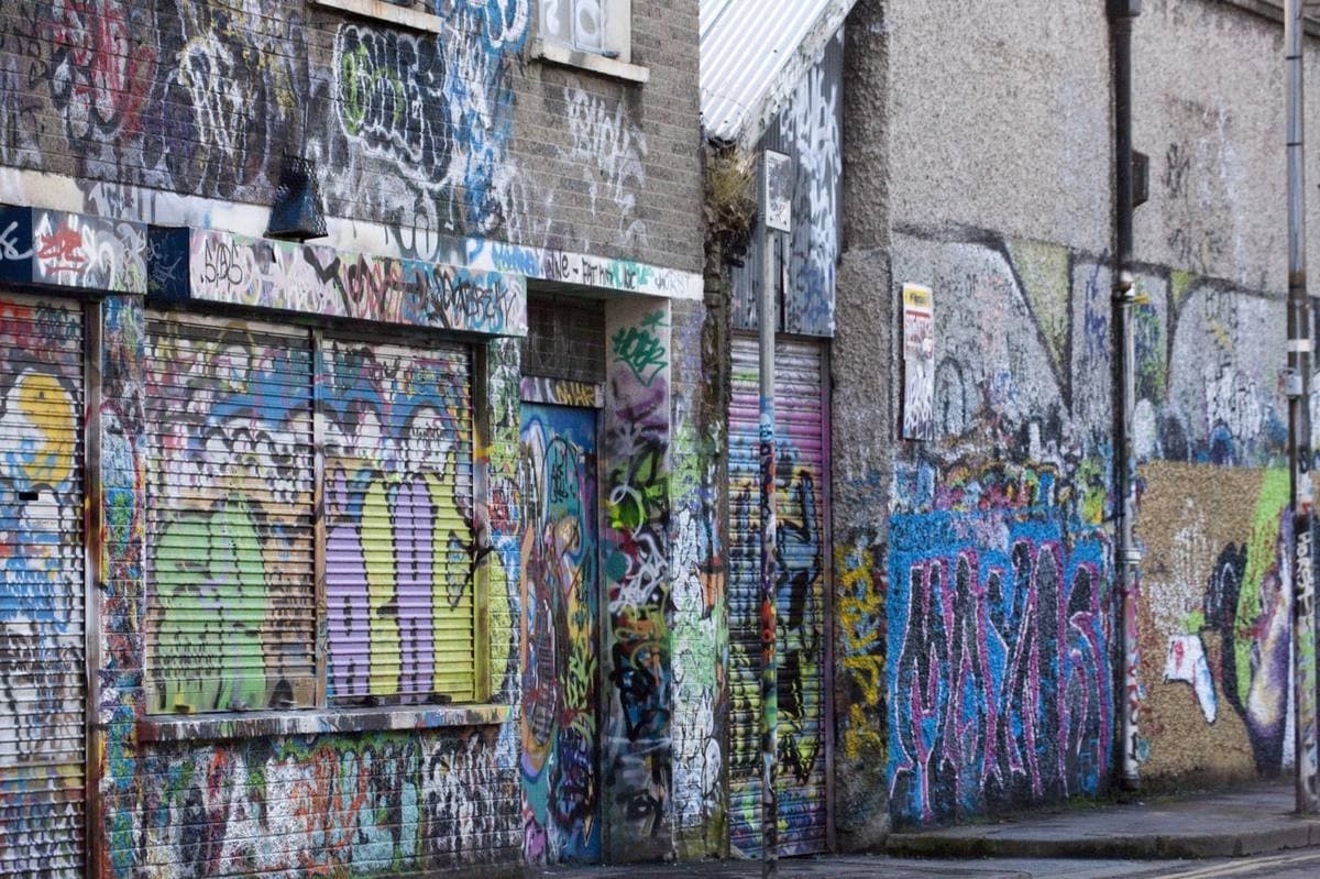 Shuttered doorways in a lane, every surface layered with spray paint and marker