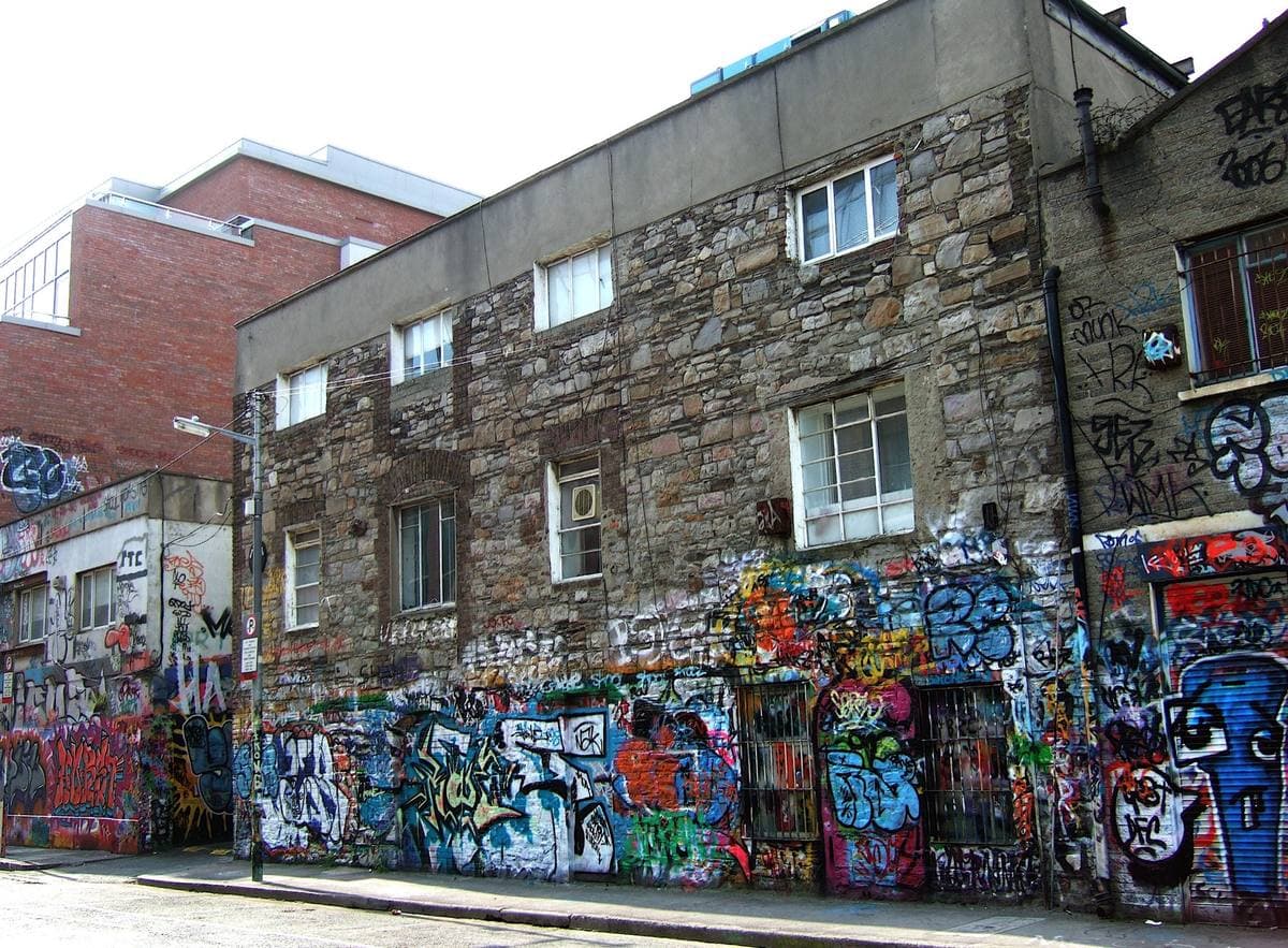 A stone warehouse whose lower walls are covered from end to end in colourful graffiti