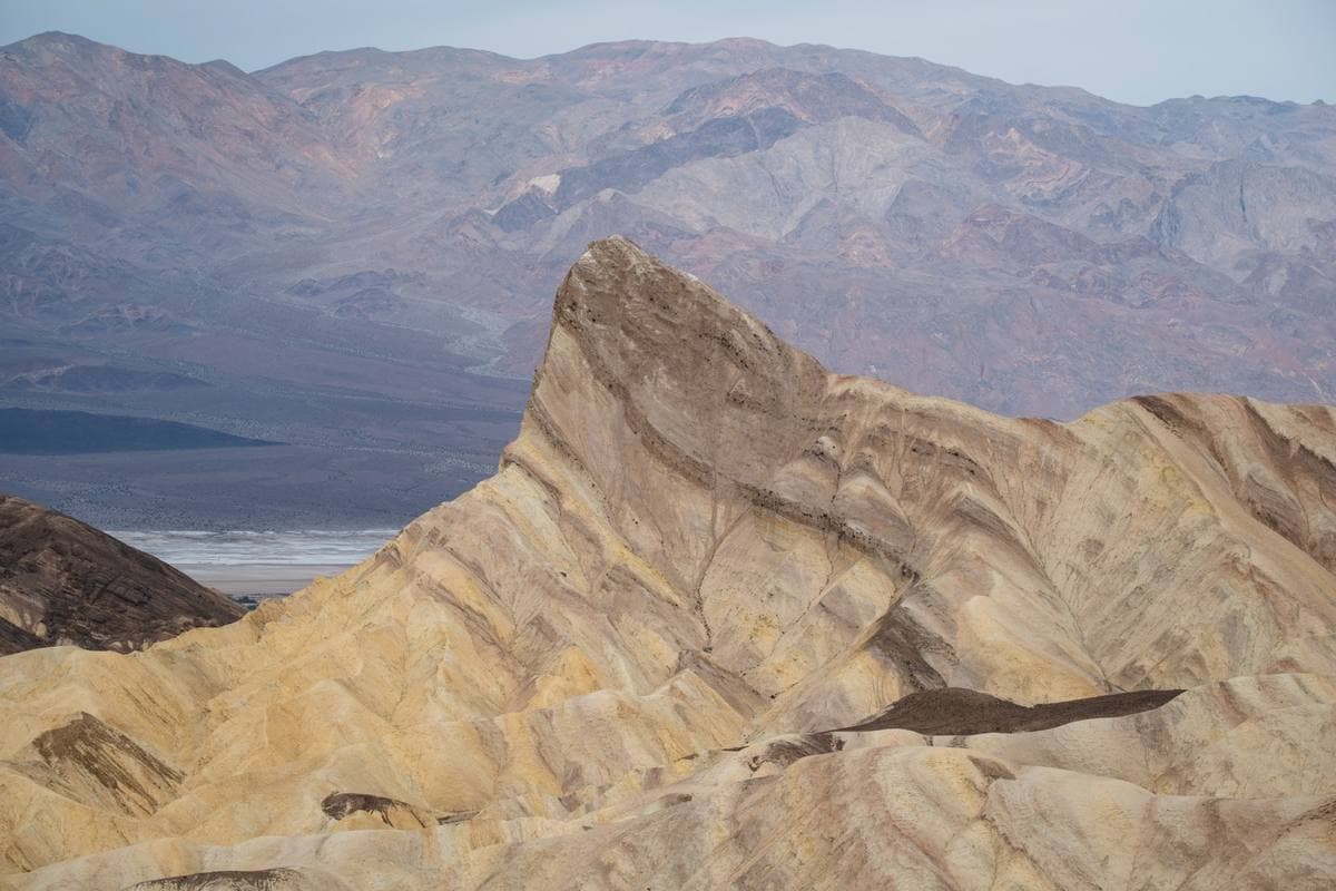 A sharp ridge of pale striped badlands in front of distant brown mountains