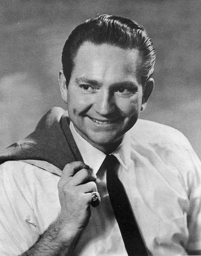 A clean-shaven Willie Nelson with short slicked hair, smiling, a jacket slung over his shoulder
