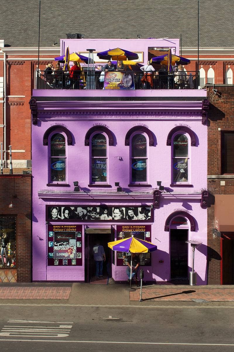 A narrow brick bar front painted bright purple, with a rooftop terrace and umbrellas