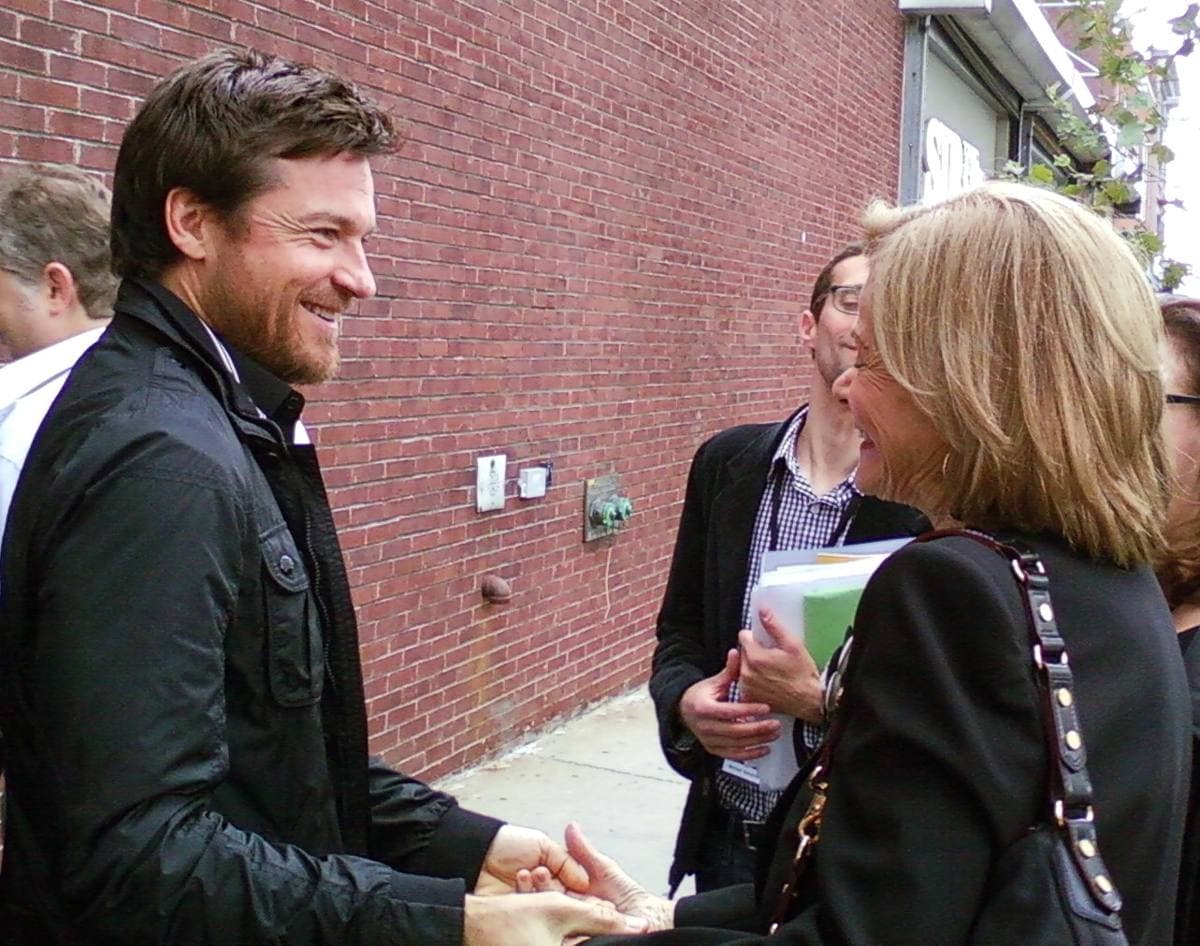 Jason Bateman smiling and holding Jessica Walter’s hands by a brick wall