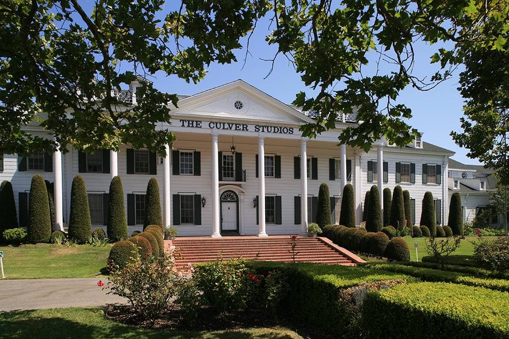 A white colonial mansion with tall columns behind a lawn