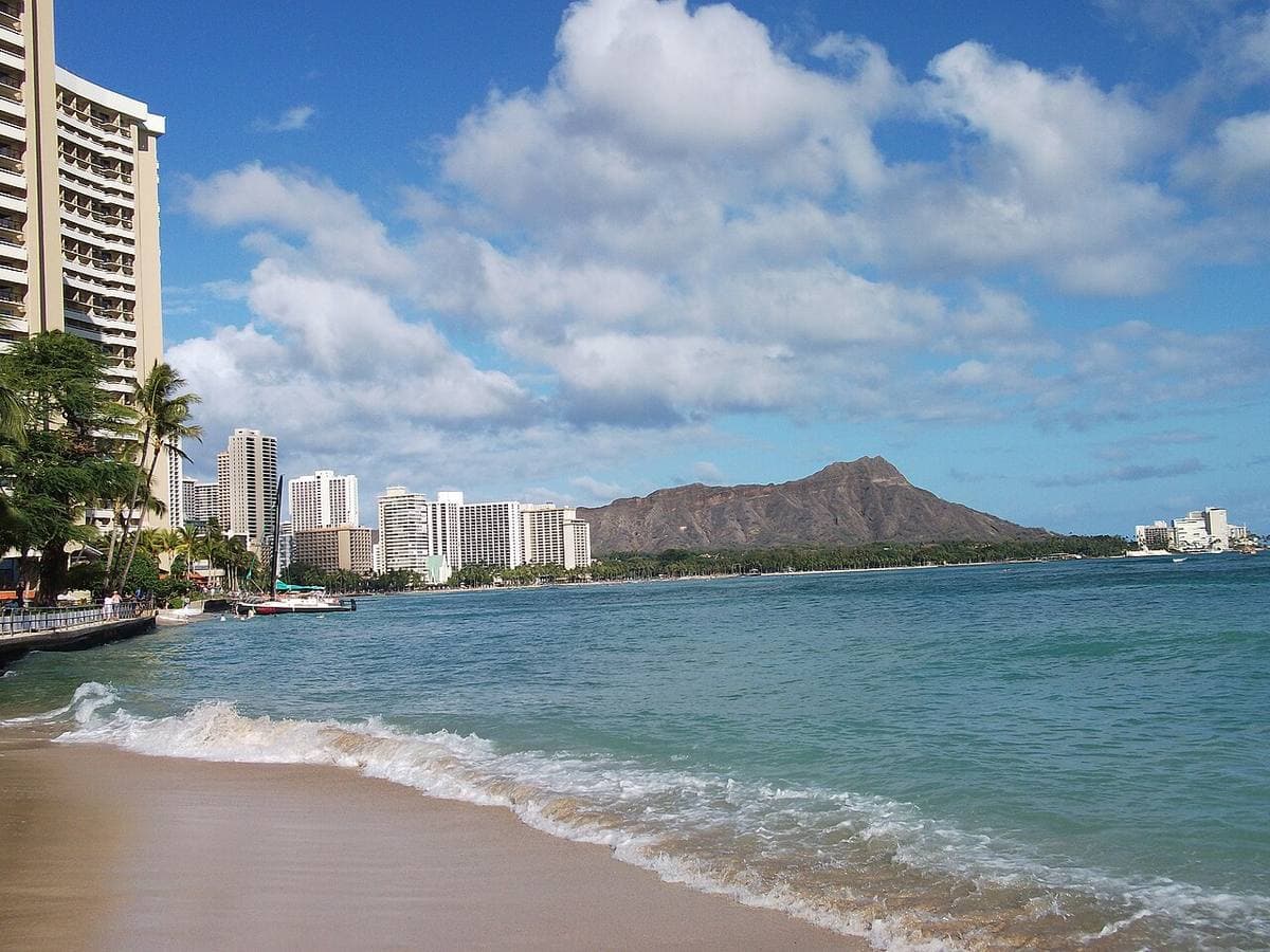 A beach with swimmers and the green ridge of Diamond Head behind