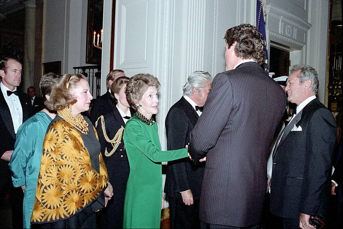A tall man in a dark suit shakes hands with Nancy Reagan in the East Room