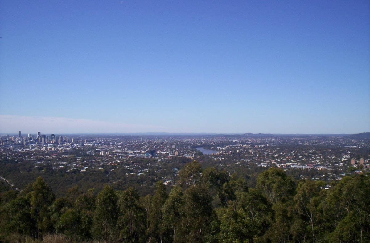 Wide view over green suburbs to the Brisbane city skyline from a hilltop