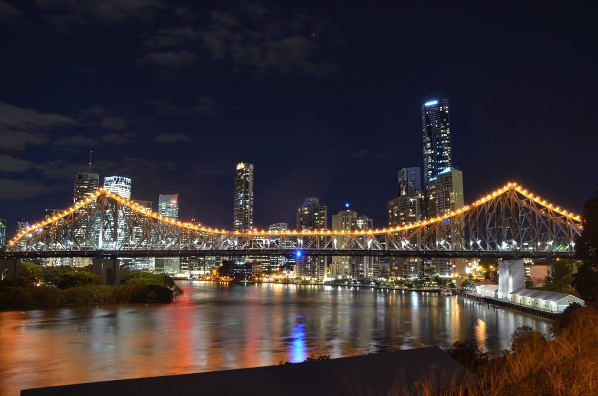 Steel cantilever bridge over the Brisbane River with city towers behind at dusk