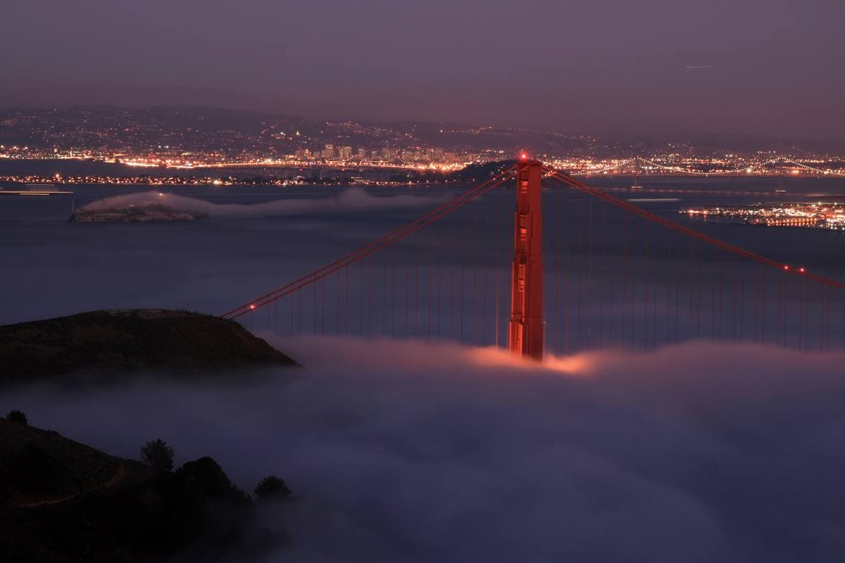 The lit Golden Gate Bridge at night with the lights of San Francisco beyond the water
