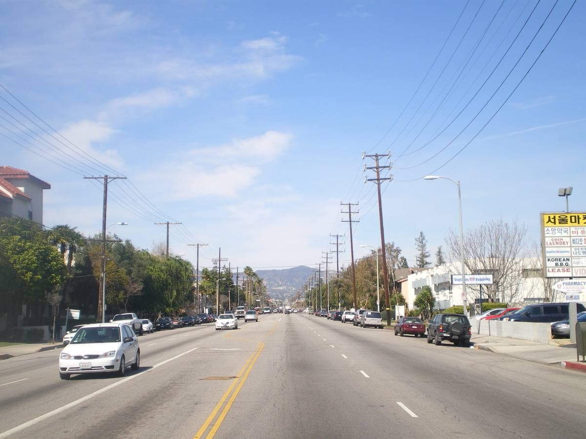 A wide Valley boulevard with palm trees and low shops