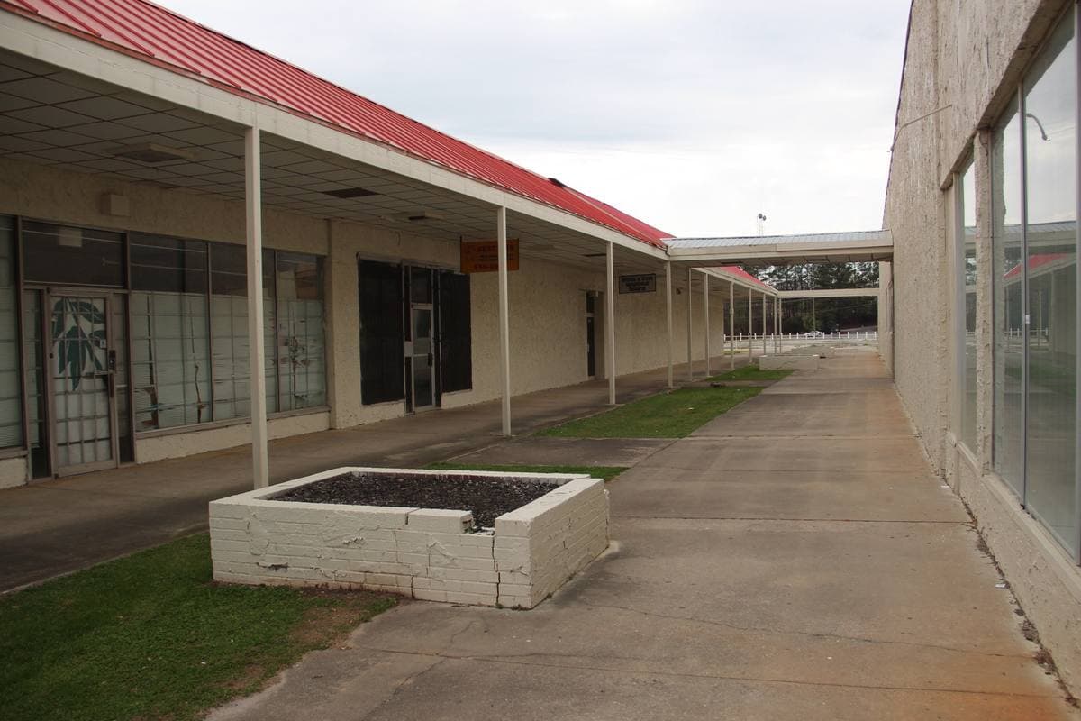 A low 1960s shopping centre with a long canopy and car park