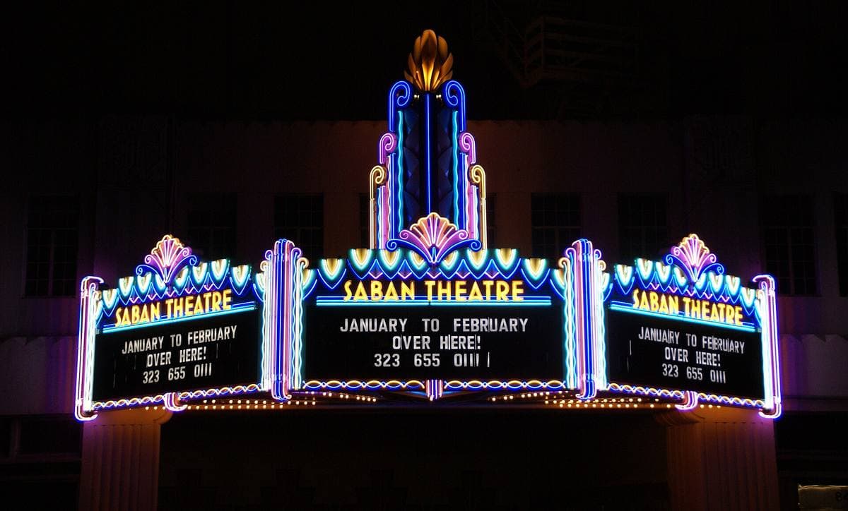 An art deco theatre tower lit up at night above Wilshire Boulevard