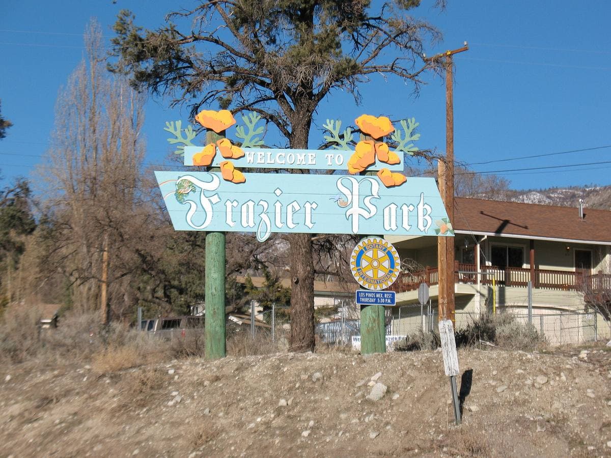 A wooden town sign among pines on a mountain road