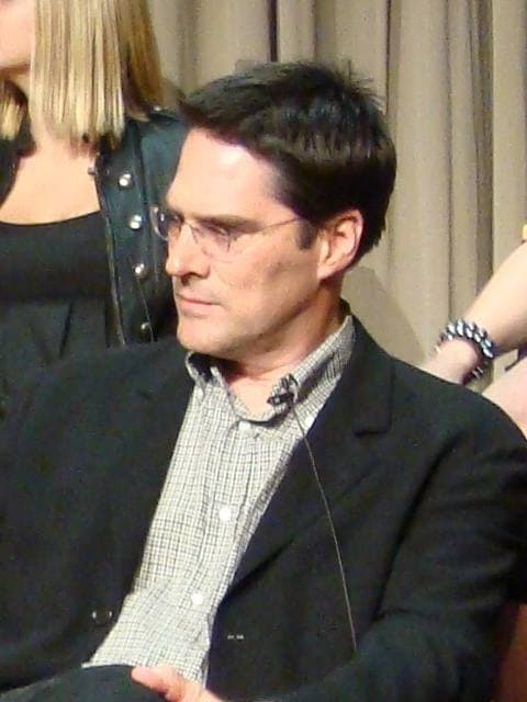 A man in a dark suit and open-necked shirt