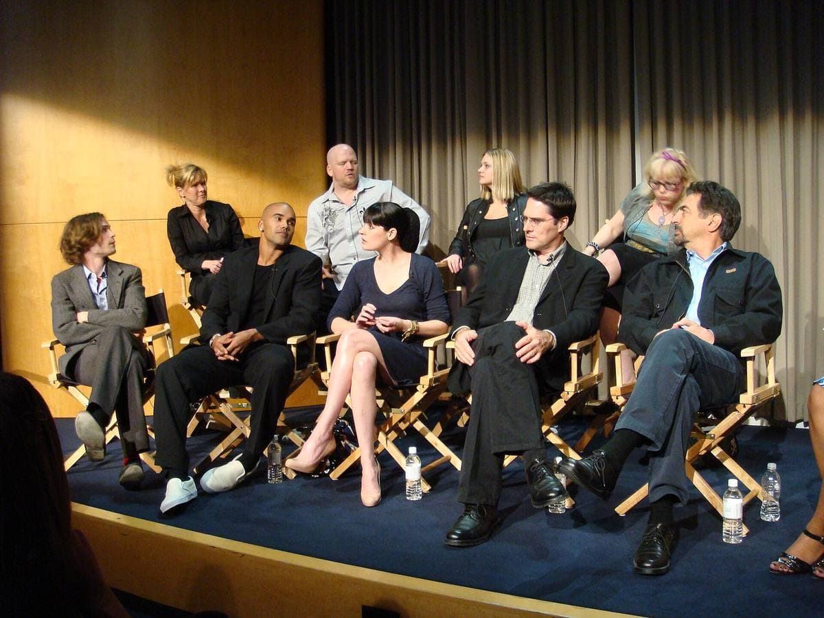 Nine people on a small stage, most in folding director’s chairs