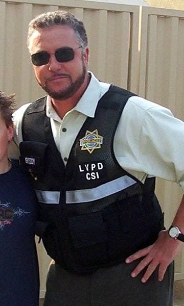 A man with short greying hair and a beard, smiling