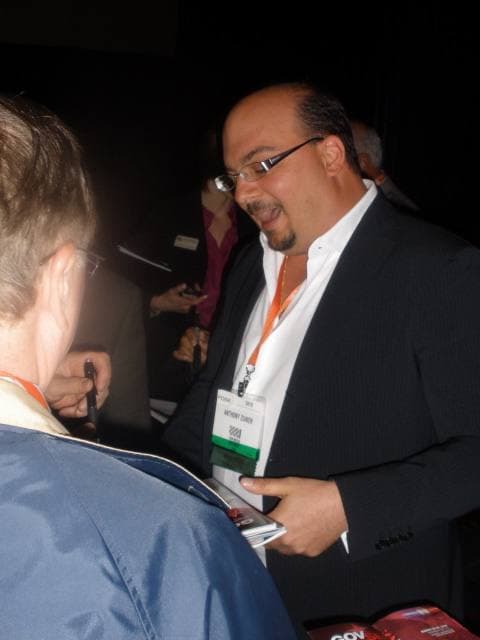 A man in a dark suit signing autographs at a table