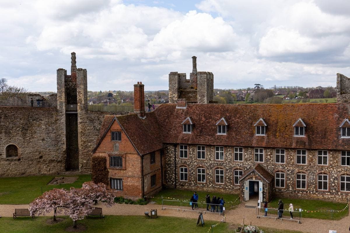 Flint curtain walls and towers around a long brick building with tall chimneys