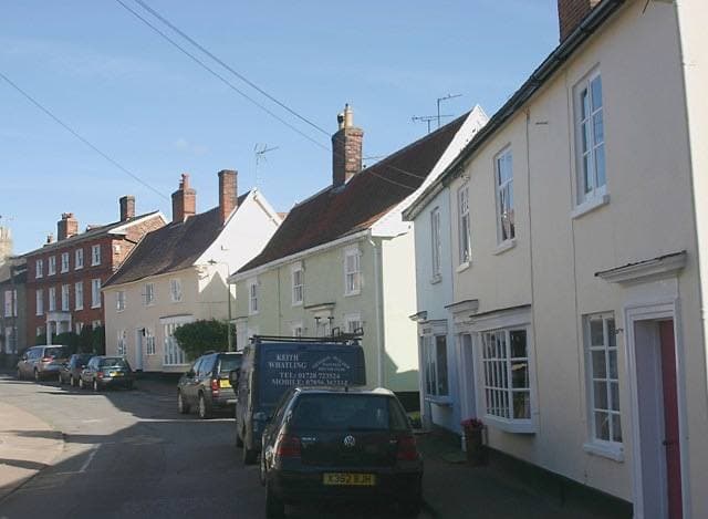A narrow street of painted terraced houses with cars parked along one side