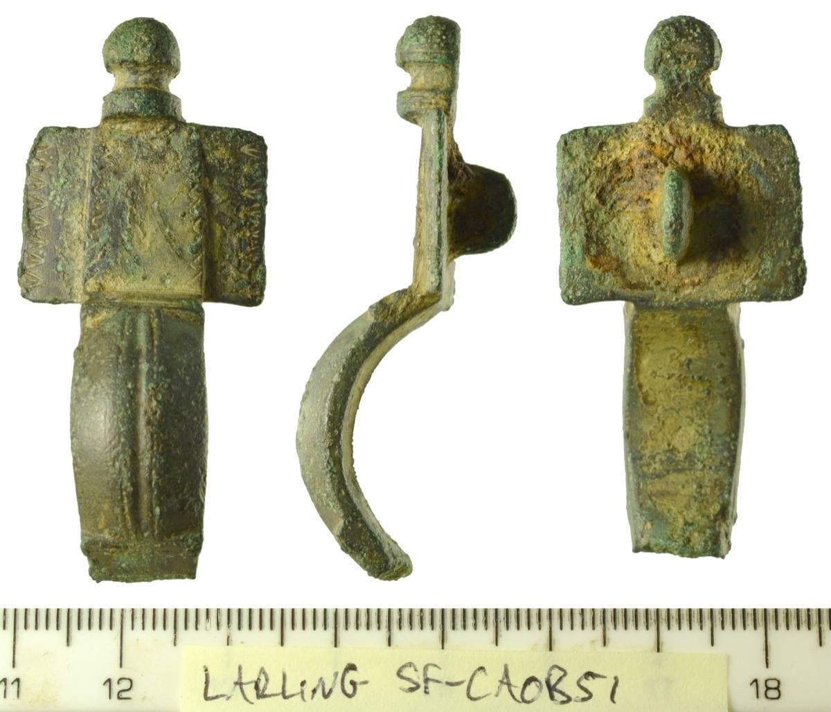 The head of a green bronze brooch with a rounded knob and grooved decoration