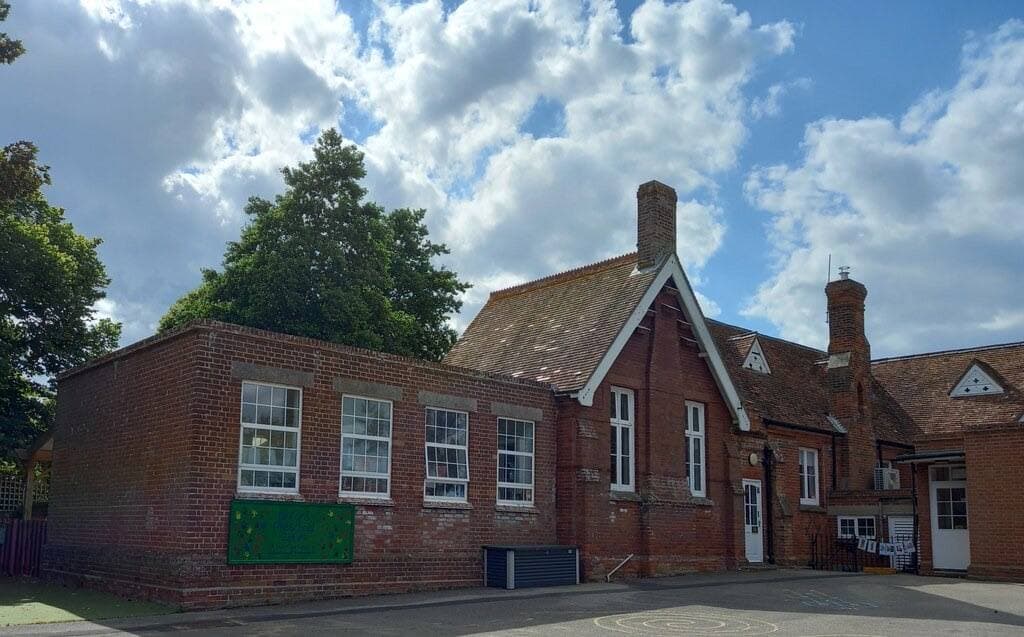 A red-brick village school with tall windows and a pitched roof under summer cloud