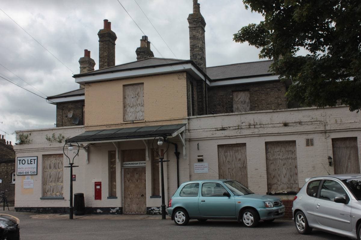 A pale two-storey Victorian station building with tall chimneys and cars outside