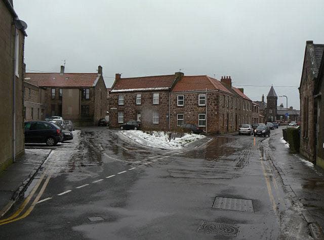 A wet road opening into a small square of brick buildings, with thawing snow