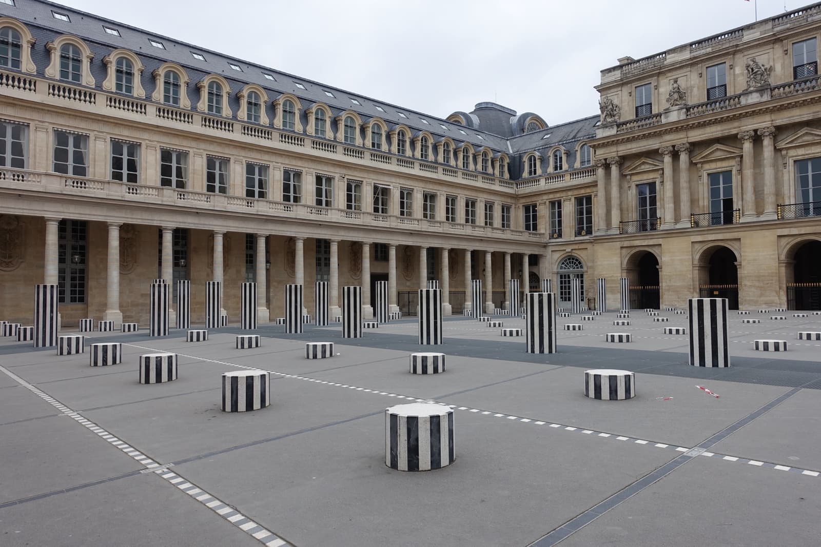 Striped black-and-white columns of different heights across a stone courtyard, arcades behind