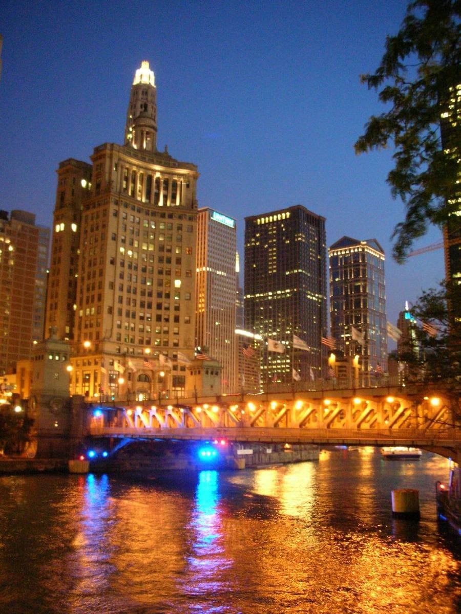 The lit Wrigley Building and the bridge reflected in the dark river