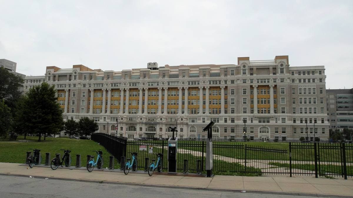 A long cream terracotta Beaux-Arts hospital front behind a lawn and a bike-share dock