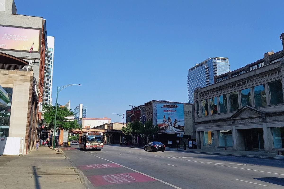 Chicago Avenue in sunshine, a bus in the distance and low brick buildings by the elevated line