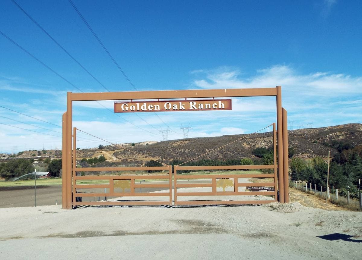 A ranch gate and sign among oak trees and dry hills
