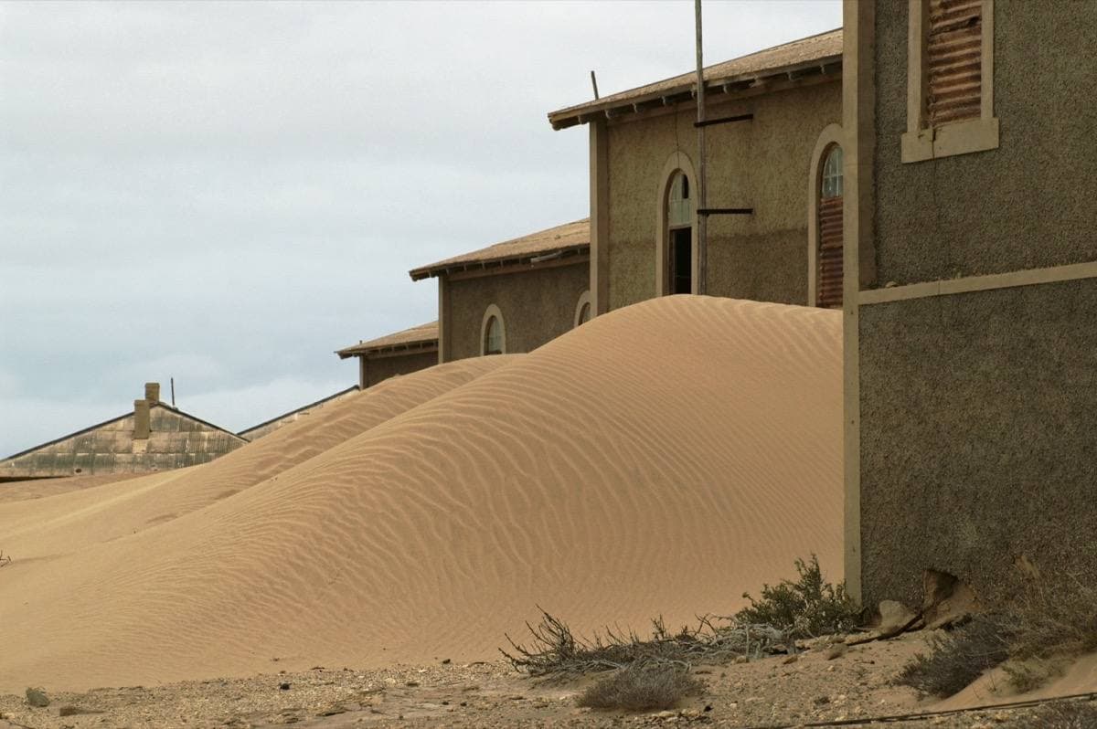 A sand dune piled against old stone houses in a desert ghost town