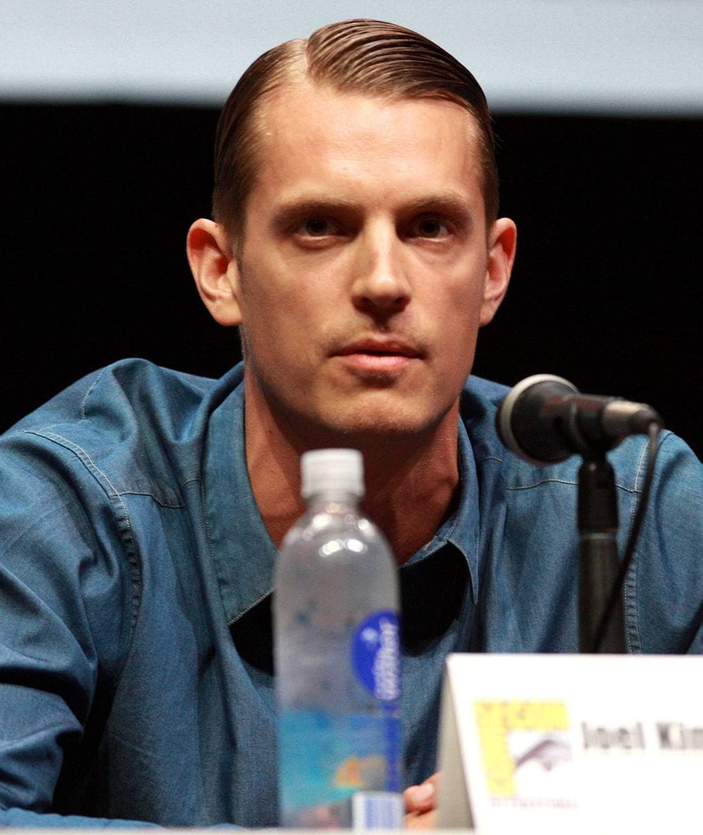 A dark-haired man in a jacket at a convention panel