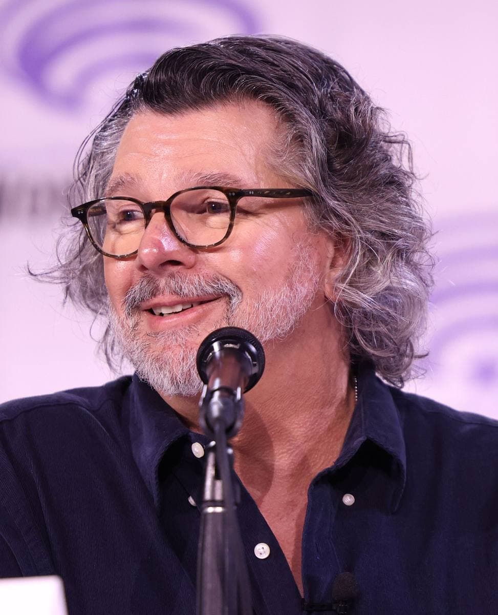 A grey-bearded man in glasses speaking into a microphone