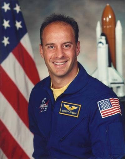 An astronaut in a blue flight suit in front of a flag