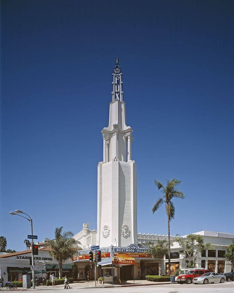 A Spanish Revival cinema with a tall white tower and a blue marquee