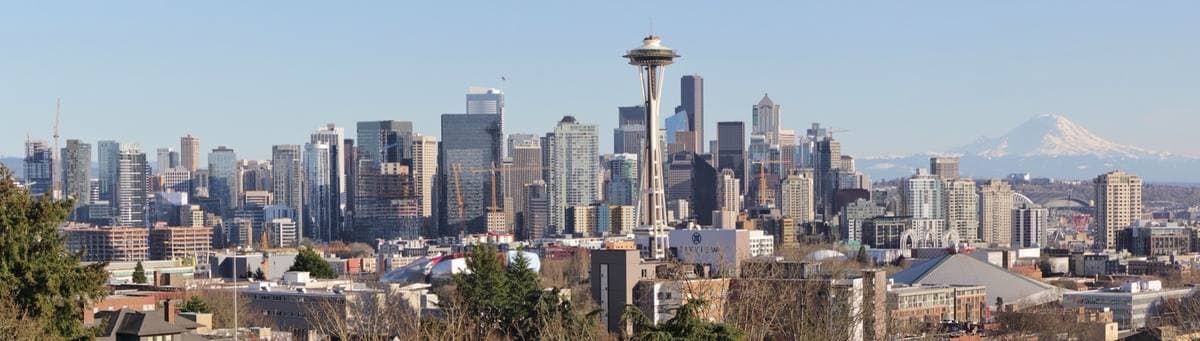 A wide skyline of downtown Seattle with the Space Needle at left and snow-capped Mount Rainier at right