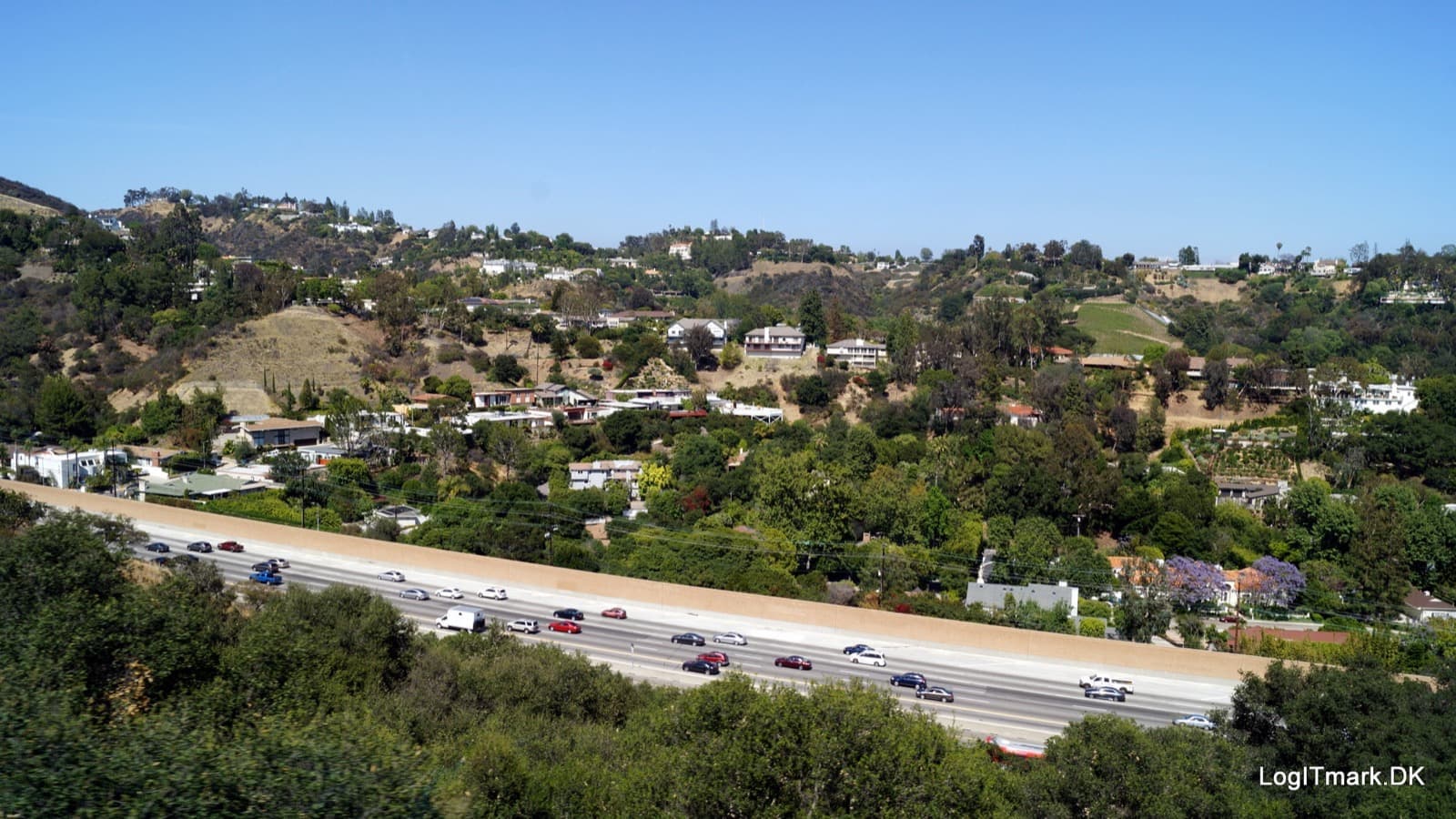 Green hillsides of large houses and trees above a busy freeway