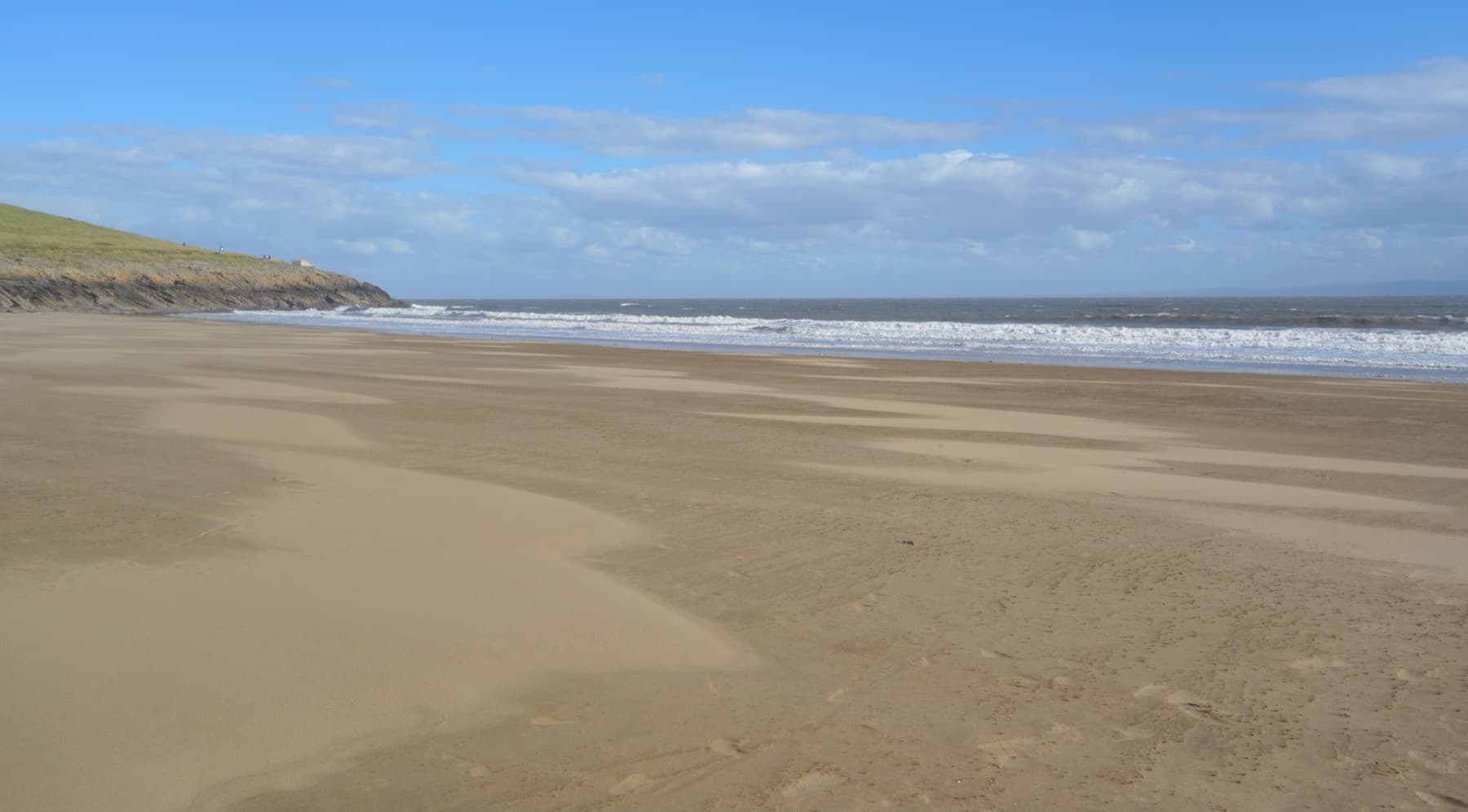 Wide wind-rippled sand running to the sea under a blue sky