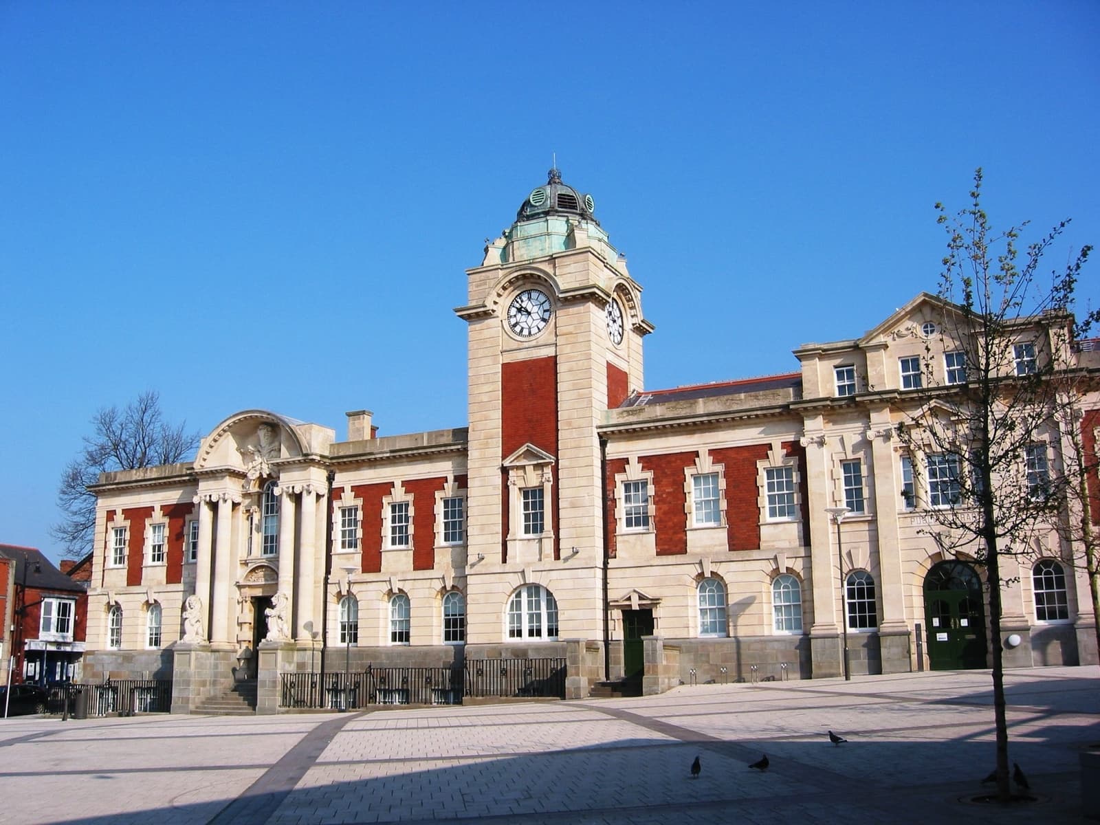 A red-brick and stone civic building with a clock tower over a paved square